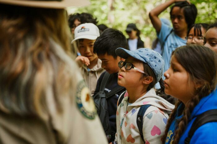 A young Asian girl wearing glasses gazes off-camera, surrounded by fellow school-aged children. 