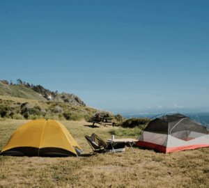 Two tents on a green plateau with a grassy hillside and blue skies in distance.