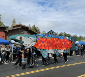 A large replica of a salmon is carried through the streets during a parade.